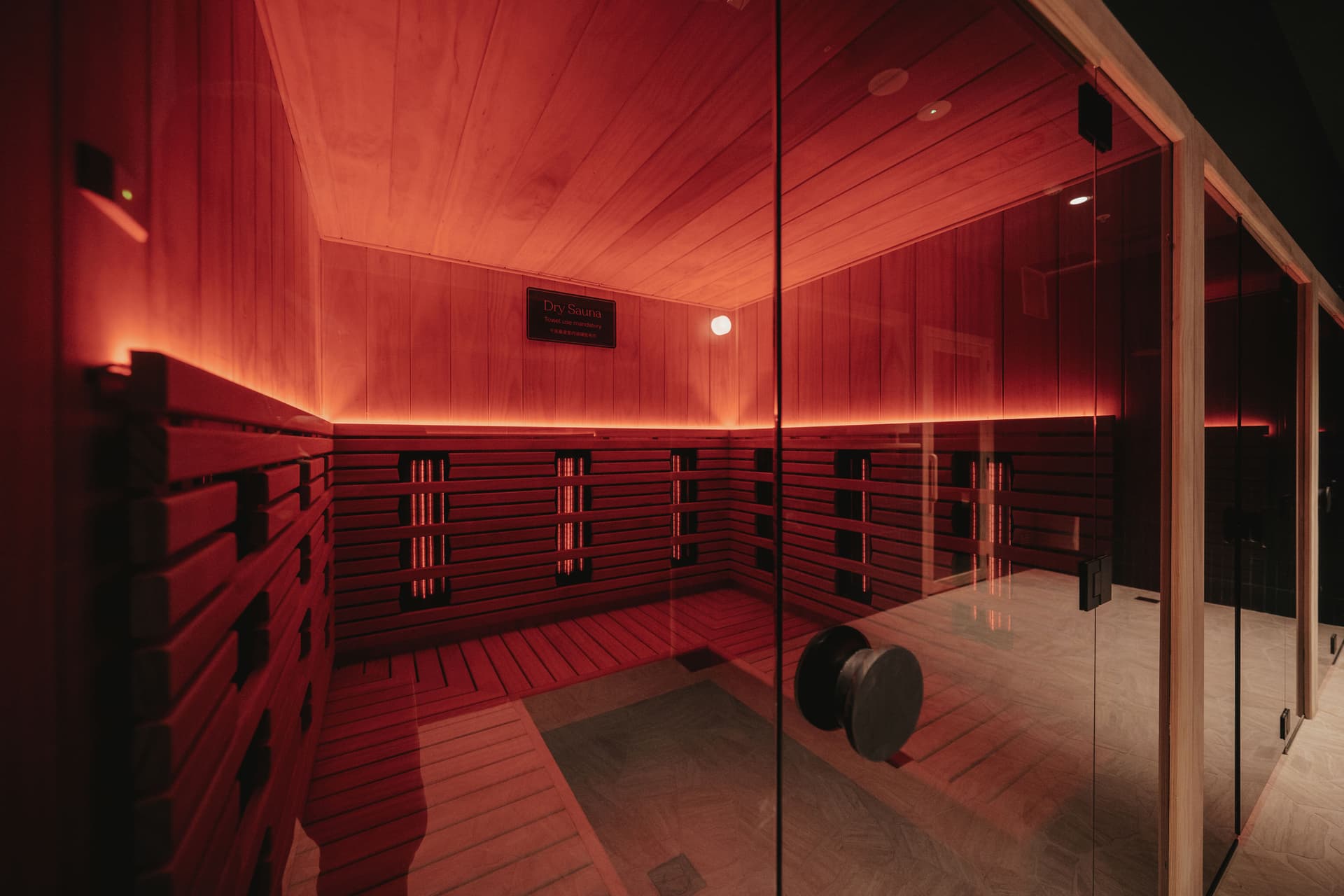 Interior of an infrared sauna cabin with slatted timber walls, glowing heater elements and a bench under warm red light