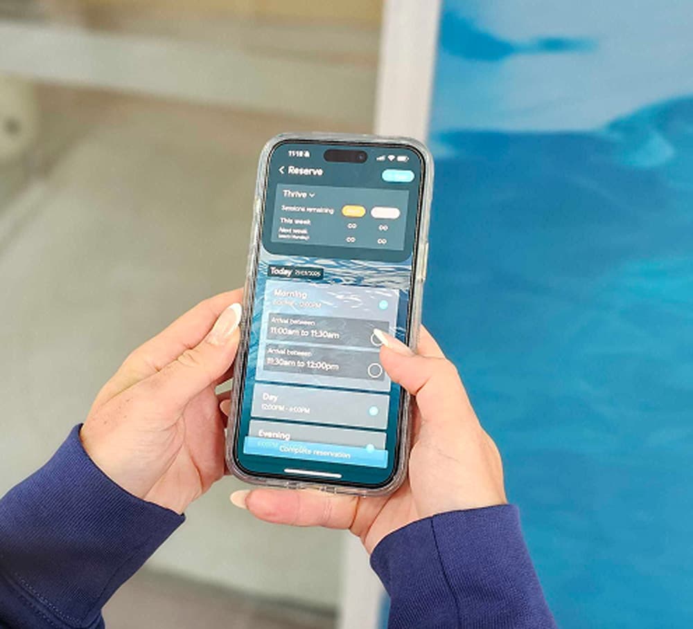 Hands holding a phone showing the XtraClubs booking screen, beside an ice bath